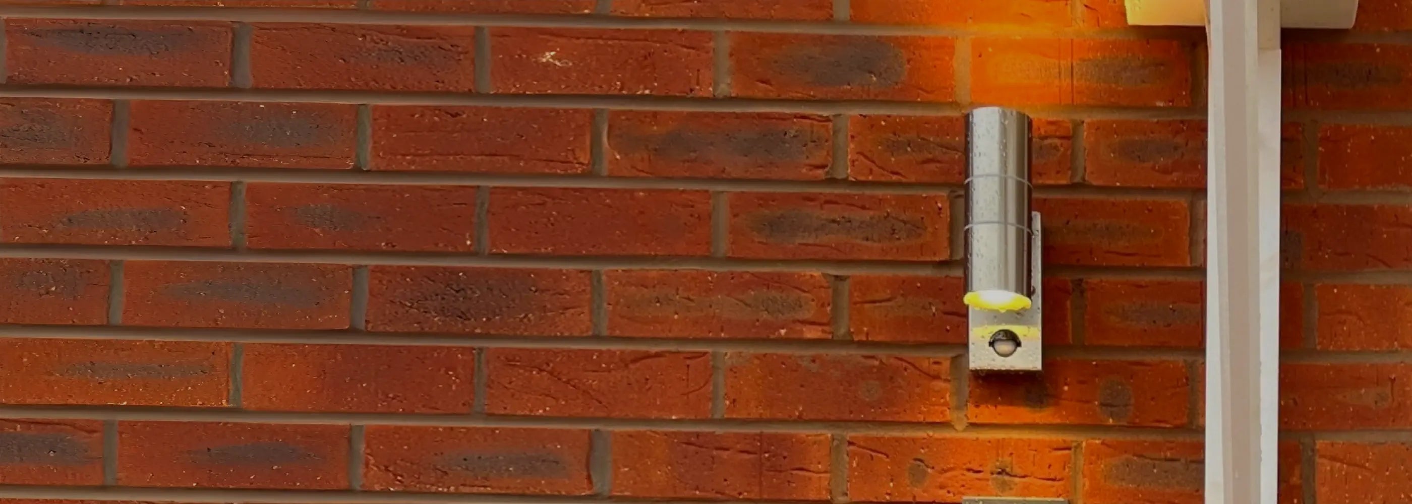 A modern house number sign displaying “No 8” in white text on a dark rectangular plaque is mounted on a red brick wall next to a sleek black door and a white vertical light fixture.