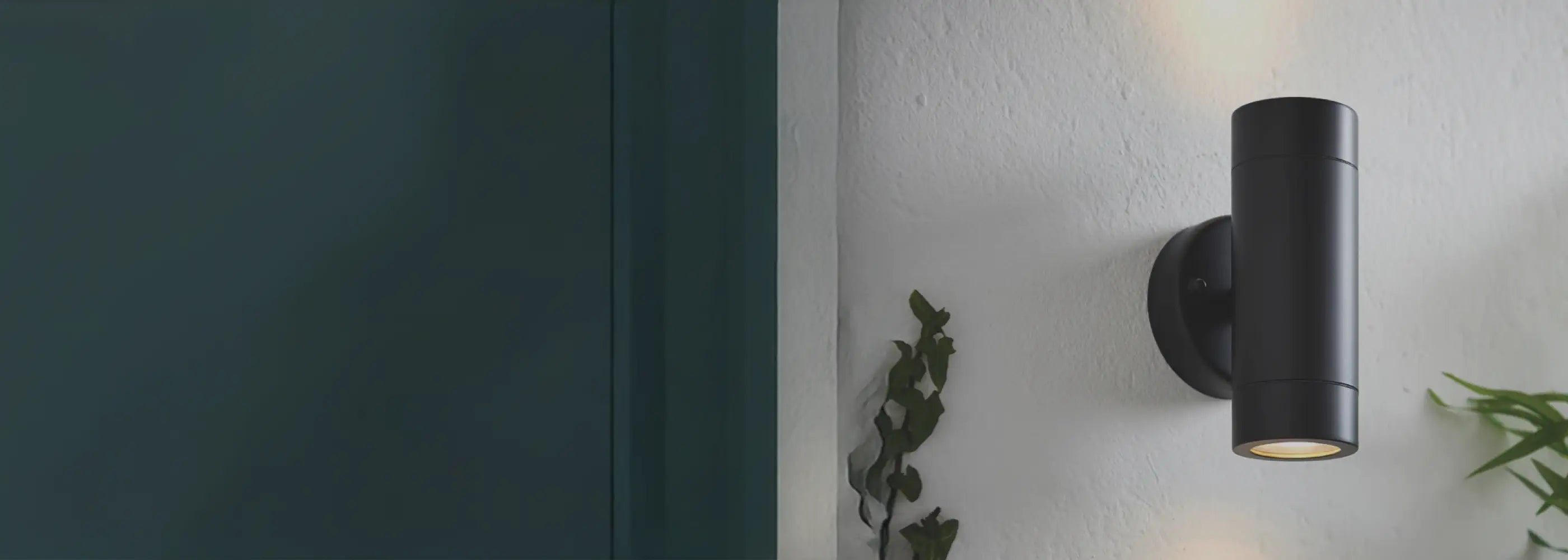a close up shot of a silver wall light turned on. the photo is taken slightly above the light, looking down into the bulb cap where the light shines through. the warm white bulb is switched on