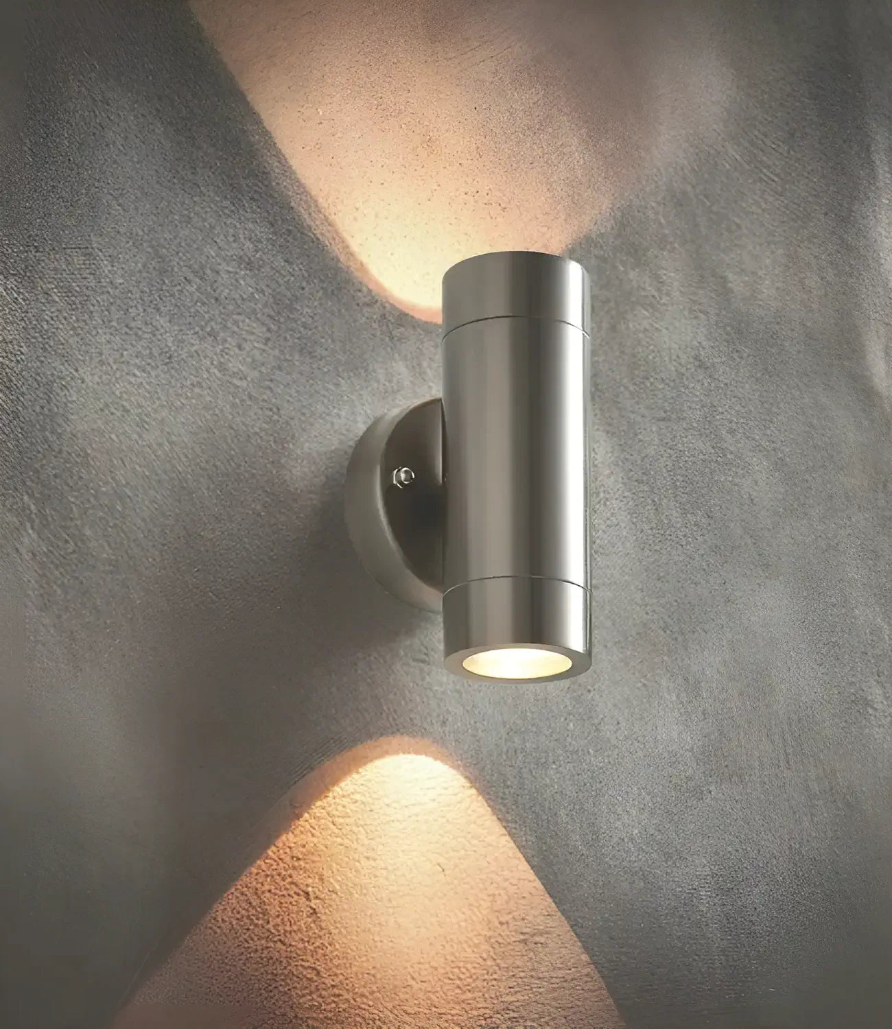 Sleek stainless steel outdoor wall light with up-and-down illumination, casting warm light against a textured grey wall.