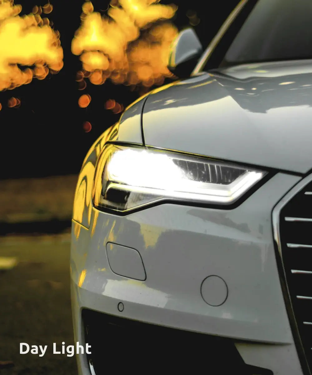 A close-up of a car’s illuminated headlight at dusk, with golden bokeh effects in the background, highlighting the bright, daylight-like lighting.