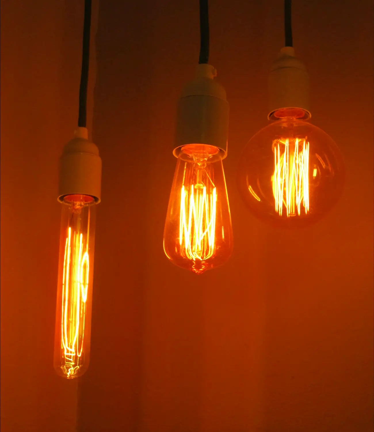 Three vintage-style filament light bulbs with warm amber glows hang from black cords against a softly lit background, creating a cozy and inviting atmosphere.