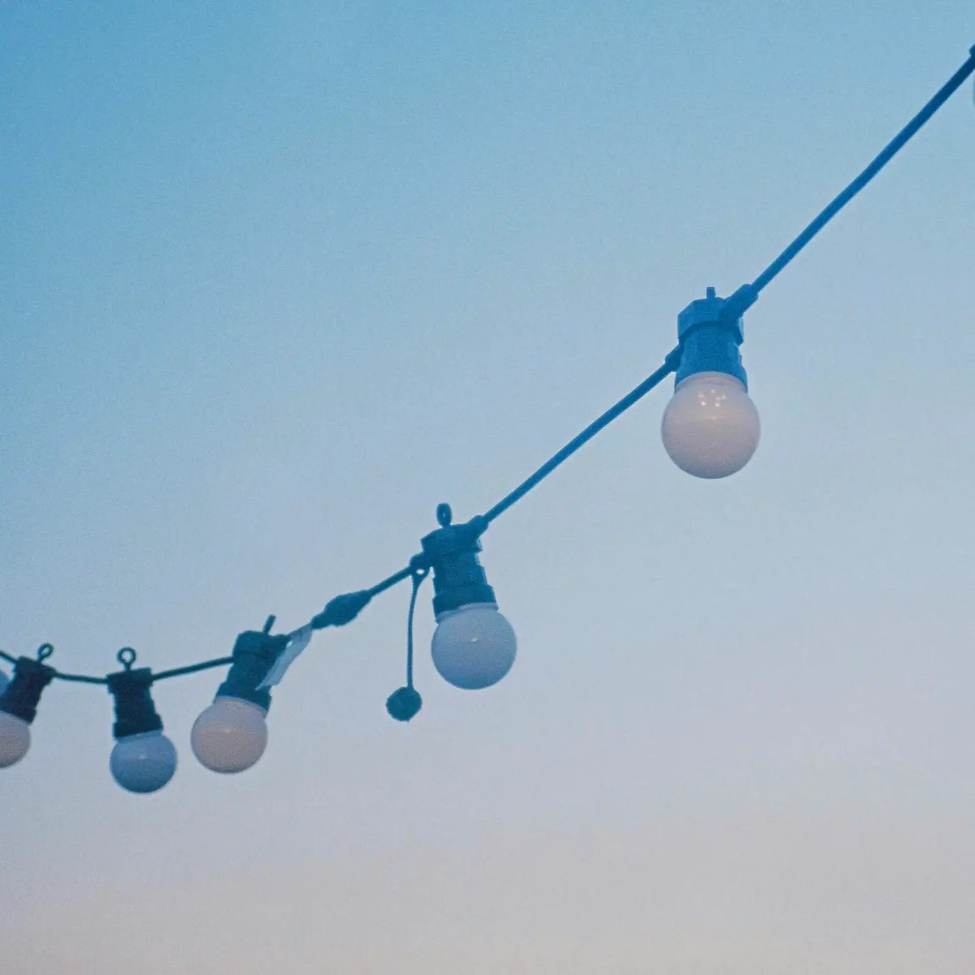 A string of decorative outdoor light bulbs hanging against a clear blue sky, creating a simple and serene ambiance.