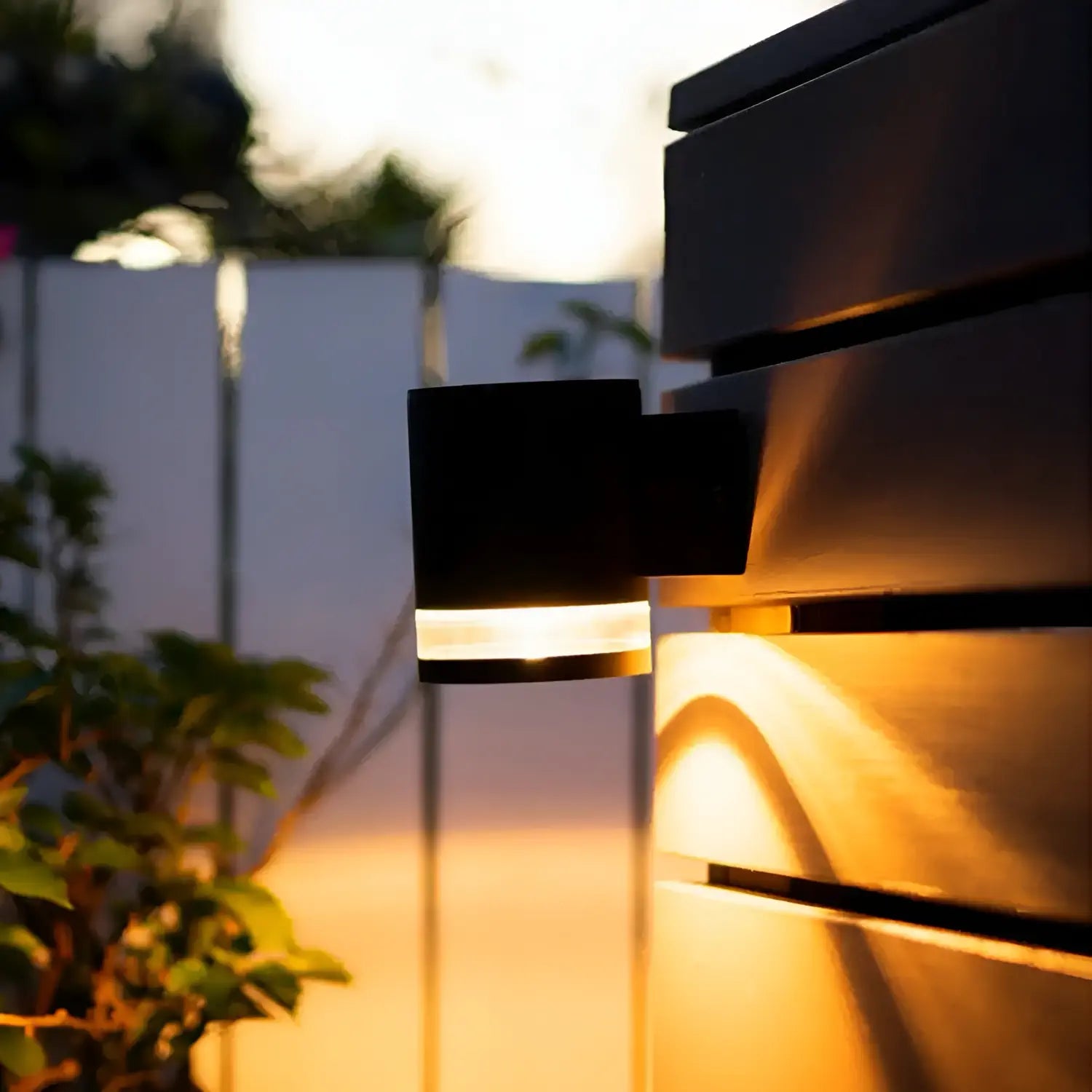 A sleek black outdoor wall light with a modern design, mounted on a horizontal panel, casting warm illumination onto the surface and surrounding area, creating a cozy evening ambiance.