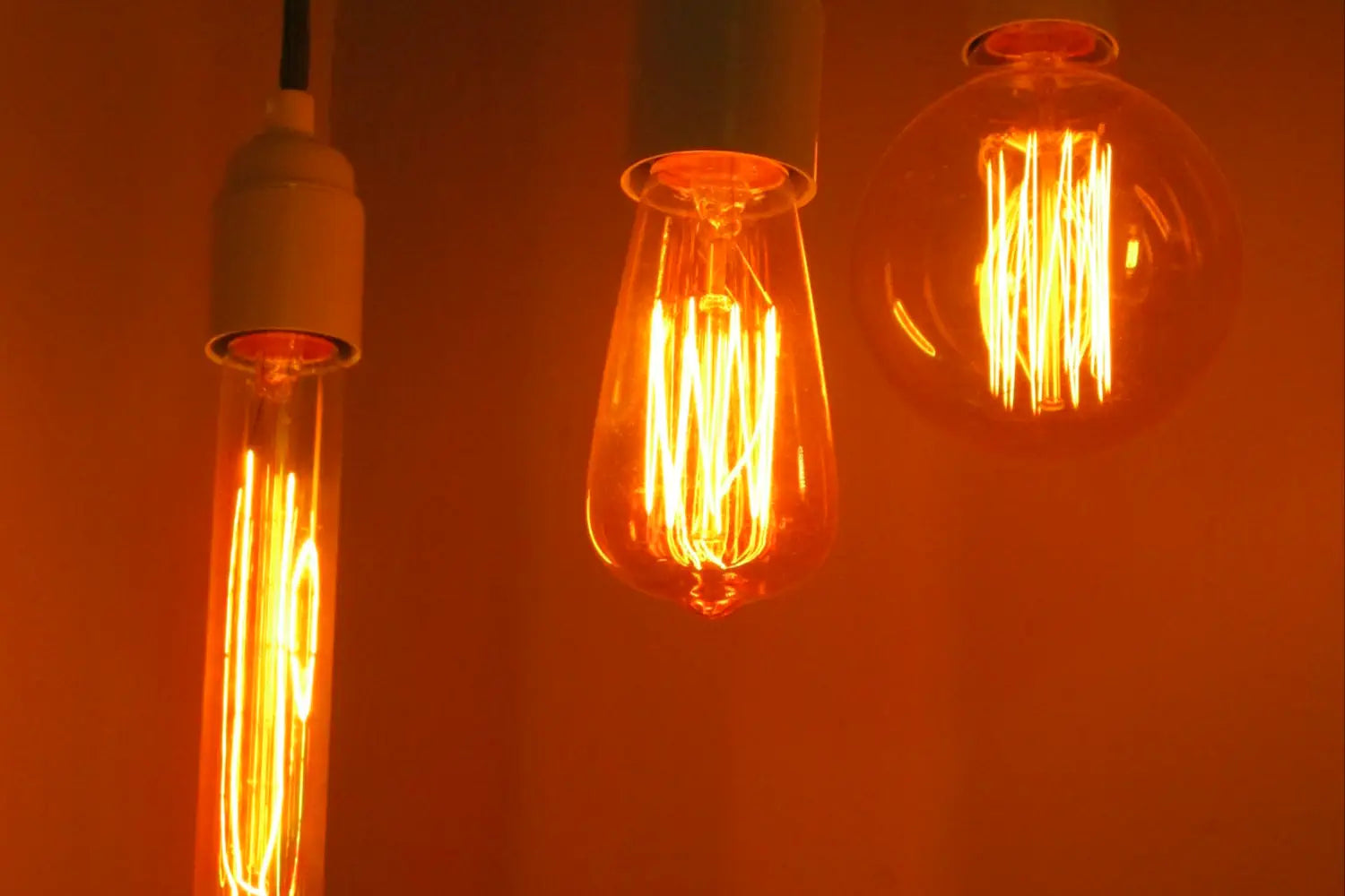 Three vintage-style filament light bulbs with warm amber glows hang from black cords against a softly lit background, creating a cozy and inviting atmosphere.
