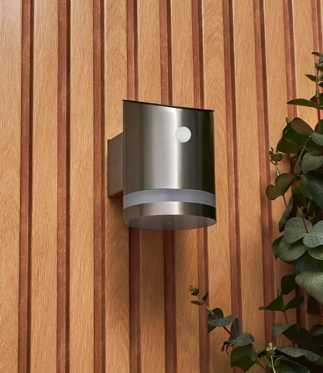 a silver solar light with a motion detector on the front. The light is mounted onto a wooden wall and is turned off