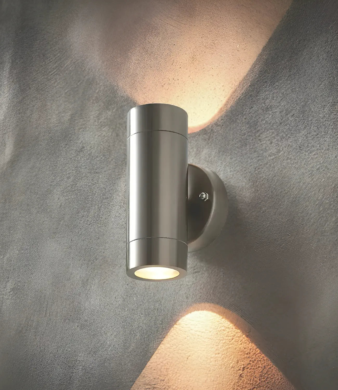 a smart, modern looking up and down wall light in stainless steel silver turned on. the light shines light upwards and downwards on the grey concrete wall the light is mounted on