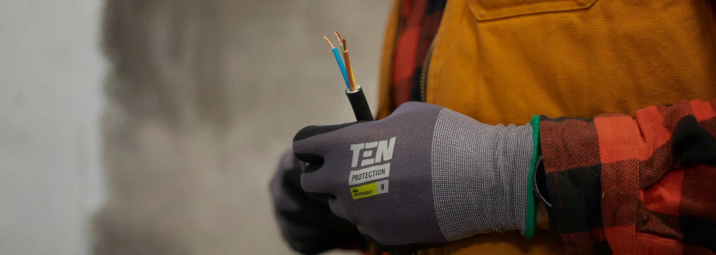 Person wearing protective gloves holding an electrical cable with exposed wires.