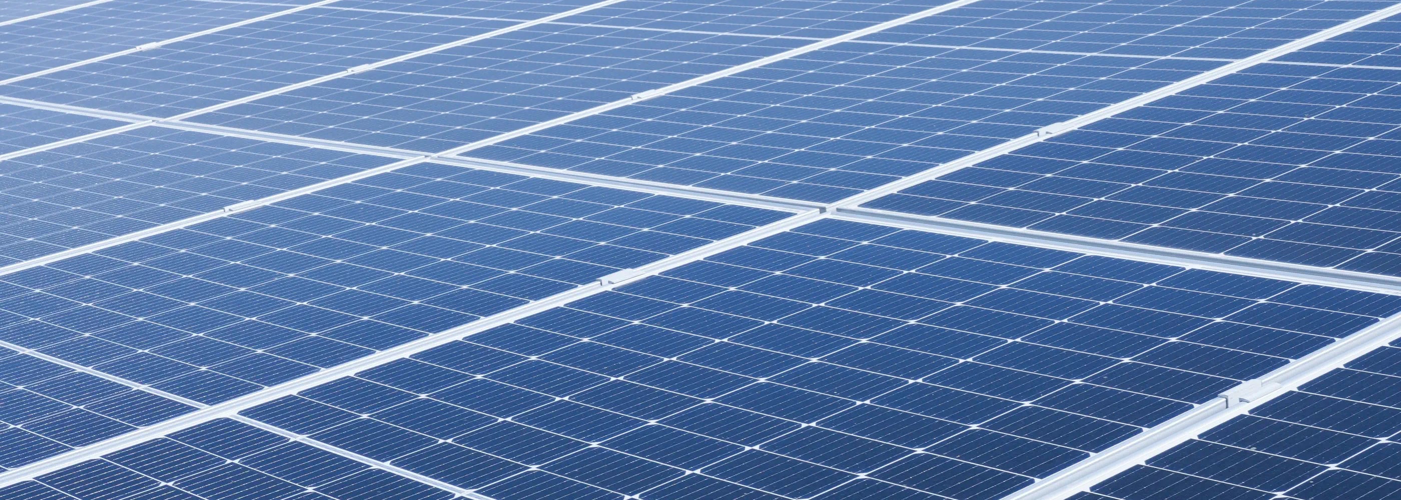 Close-up of blue solar panels capturing sunlight, showing the fine grid pattern and reflective surface of the photovoltaic cells.