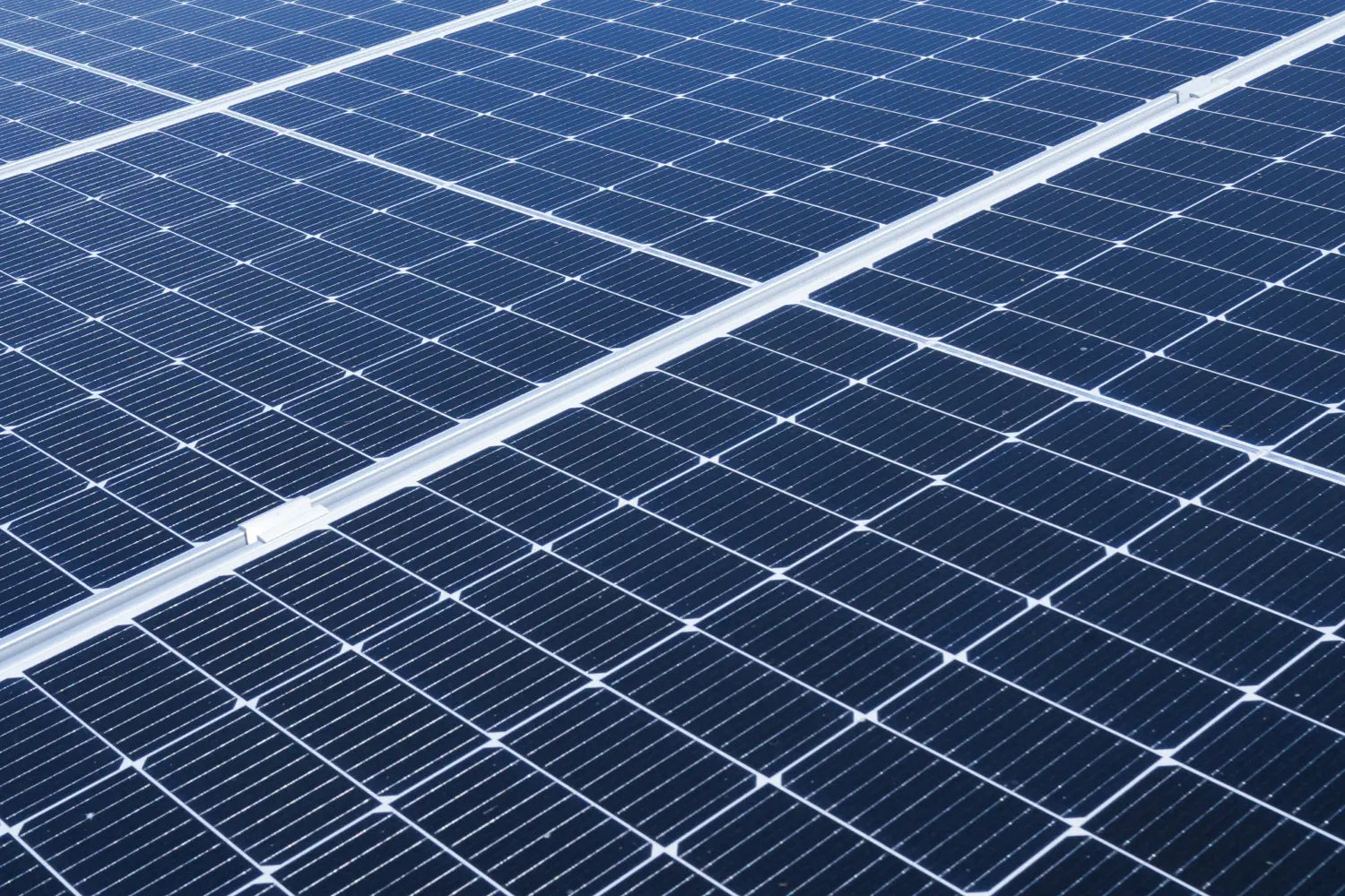 Close-up of blue solar panels capturing sunlight, showing the fine grid pattern and reflective surface of the photovoltaic cells.