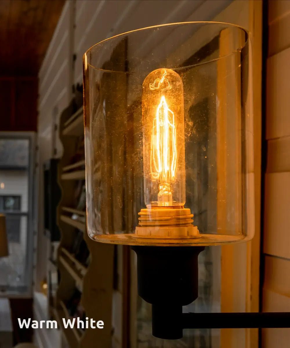 A glowing warm white Edison-style bulb encased in a clear glass sconce, creating a cozy and inviting ambiance within a wood-panelled room.