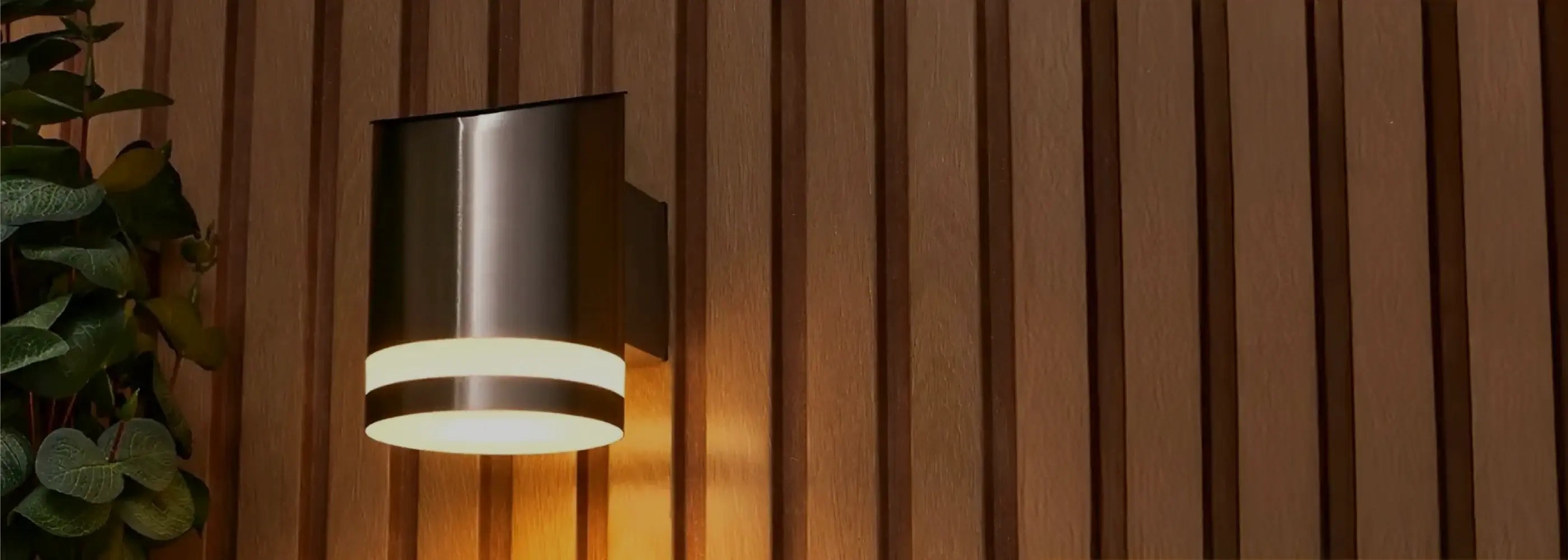 a silver solar light on a wooden panel wall next to green bushes
