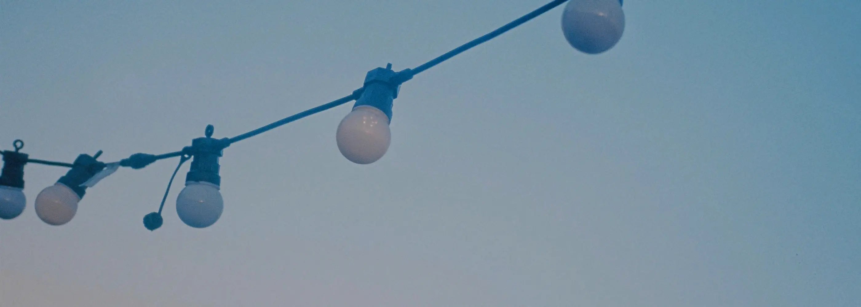 a string of 5 light bulbs against a pale blue evening sky