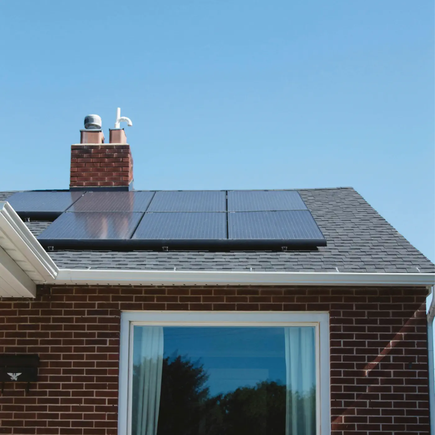 A brick house on a sunny day with a grey slate tiled roof with 7 black solar panels covering the majority of the roof