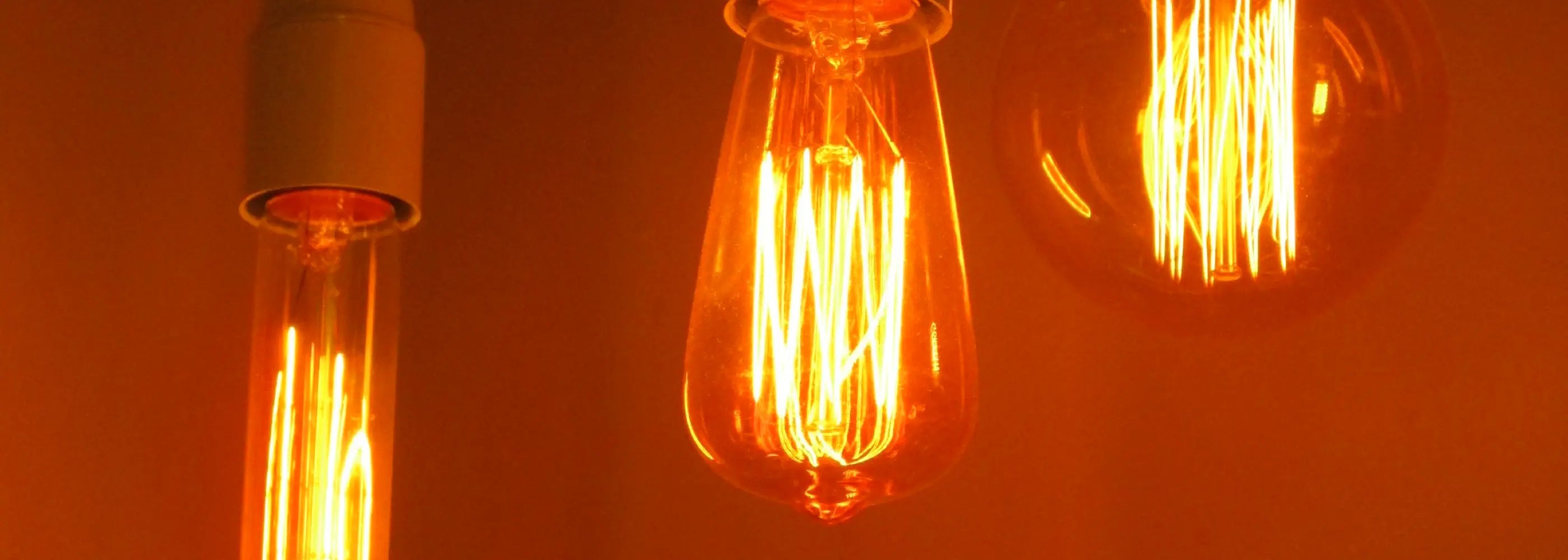 Three vintage-style filament light bulbs with warm amber glows hang from black cords against a softly lit background, creating a cozy and inviting atmosphere.